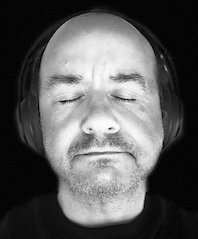 A man with closed eyes and headphones on his ears.